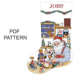 May include: A cross-stitch pattern for a Christmas stocking featuring Santa Claus painting toys. The stocking is white with a red "JOHN" at the top. The scene includes a shelf of toys, a Christmas tree, and the text "PDF PATTERN".