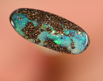 May include: A dark brown and green opal cabochon with a unique pattern of iridescent colors. The opal is set in a silver ring.