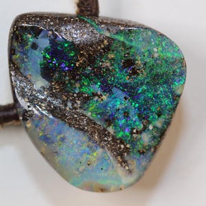 May include: A dark brown and black opal pendant with green, blue, and white iridescent flashes. The pendant is attached to a brown leather cord.