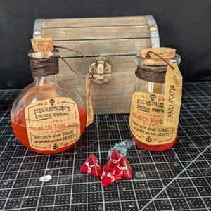 May include: Two glass bottles filled with red liquid and labeled "pickemup's choice brews" and "Health Potion" with the text "When you're almost TOAST, we got what you need MOST!"  The bottles are sitting on a black and white checkered surface with red dice.