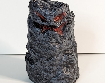 May include: A dark gray rock with a red, orange, and yellow paint design. The rock is textured and has a rough surface.