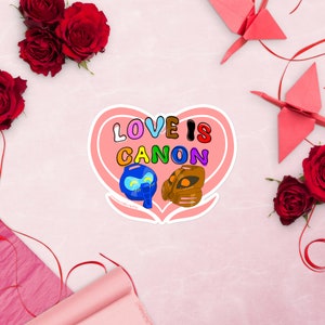 Op de afbeelding: Een roze sticker in de vorm van een hart met de tekst "LOVE IS CANON" in regenboogkleuren. Twee cartoonfiguren zijn in het hart afgebeeld, een blauwe en een bruine.