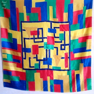 May include: A yellow silk scarf with a geometric pattern in red, blue, green, and gold. The scarf has the text "French Silk Scarf" in the center.