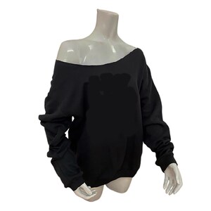 Puede incluir: Sudadera negra con hombros descubiertos. La parte superior de manga larga tiene un cuello ancho que expone un hombro. La sudadera se muestra en un maniquí. La tela parece ser un material suave y de peso medio.