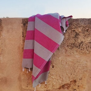 Könnte beinhalten: Ein rosa-graues gestreiftes Strandtuch, das über eine Steinmauer gelegt ist.