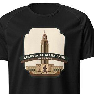 May include: Black t-shirt with a brown and beige graphic of a building and a runner. The graphic says "Louisiana Marathon 26.2 - 2026".