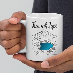 Puede incluir: Taza de cerámica blanca con un dibujo de línea negra de un volcán y un lago azul. El texto "Kawah Ijen" está impreso en negro en la taza.