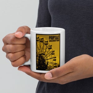 May include: White ceramic mug with a black and yellow image of a Ferris wheel at the Pripyat Amusement Park in Ukraine. The text "Pripyat Amusement Park" is printed in black on the mug.