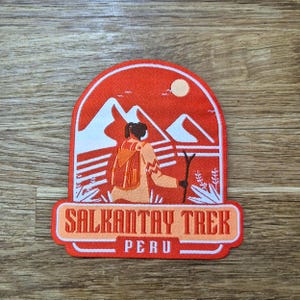 May include: A red, white, and orange embroidered patch with a hiker in the mountains. The patch says "Salkantay Trek Peru".