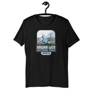May include: Black t-shirt featuring a graphic of a blue lake and a tree in a grey and white mountain landscape. The text "Kawah Ijen National Park Indonesia" is below the graphic.