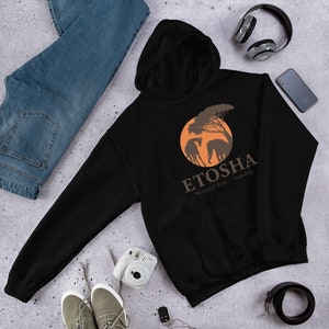 Peut inclure: Sweat-shirt à capuche noir avec un graphique circulaire orange représentant une silhouette de girafe et d'éléphant devant un arbre. Le texte "ETOSHA National Park - Namibia" est imprimé sous le graphique.