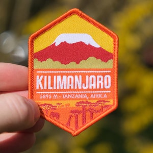 Puede incluir: Parche bordado naranja y amarillo con un pico de montaña blanco y el texto "KILIMANJARO 5895 m - TANZANIA, ÁFRICA".