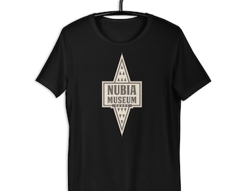 May include: Black t-shirt with a geometric design and the text "NUBIA MUSEUM EGYPT" in a rectangular frame. The design is in shades of beige and white. The shirt is hanging on a black hanger.