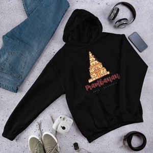 Peut inclure: Sweat-shirt à capuche noir avec un graphique du temple de Prambanan à Java, en Indonésie. Le texte "Prambanan" est écrit en cursive brune avec les mots "Java, Indonésie" écrits en plus petit en dessous.