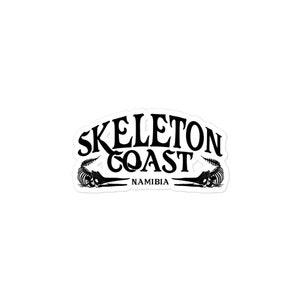 May include: Black and white sticker with the text "Skeleton Coast" in a stylized font. Below the text is the word "Namibia". The sticker features two skeletal crocodile silhouettes.