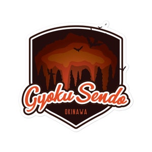May include: A sticker featuring a shield design with the words "Gyoku Sendo" in orange script. The shield has a dark brown background with an orange and brown cave illustration and several bat silhouettes. The word "OKINAWA" is below the script.