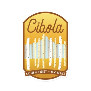 May include: A sticker featuring the text "Cibola" in a stylized font, above a graphic of birch trees. The sticker has a brown border and a yellow background. The text "National Forest - New Mexico" is at the bottom.