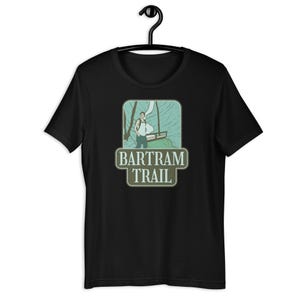 Pode incluir: Camiseta preta com um gráfico verde e azul de uma pessoa caminhando na Trilha Bartram.