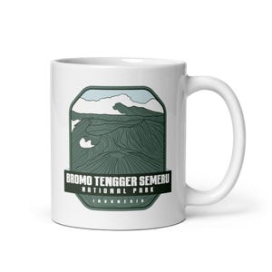 May include: White ceramic mug with a green and blue illustration of a mountain range. The text "Bromo Tengger Semeru National Park Indonesia" is printed on the mug.