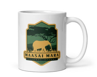 May include: White ceramic coffee mug with a green and gold logo that says "Maasai Mara National Reserve Kenya" and features a silhouette of an elephant in front of a tree.