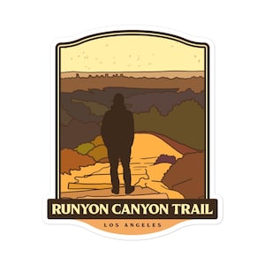 May include: A sticker featuring a retro illustration of a person standing on a trail overlooking a city skyline. The text "Runyon Canyon Trail Los Angeles" is at the bottom of the sticker.