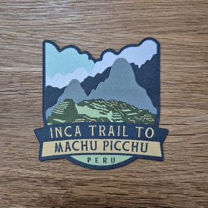 May include: A dark blue and green embroidered patch with a mountain scene and the text "Inca Trail to Machu Picchu, Peru".