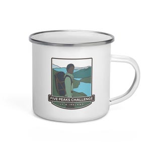 Pode incluir: Caneca de acampamento de esmalte branco com um gráfico de uma pessoa fazendo caminhadas com uma mochila na frente de uma cordilheira. O texto "Five Peaks Challenge UK & Ireland" está impresso na caneca.