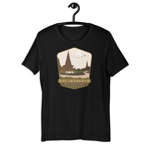 Peut inclure: T-shirt noir avec un motif brun et or du parc national de Doi Inthanon en Thaïlande. Le motif représente un temple et une chaîne de montagnes.