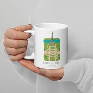 May include: White ceramic mug with a graphic of the Eiffel Tower and the Champ de Mars in Paris, France. The text "Champ de Mars, Paris, France" is printed on the mug.