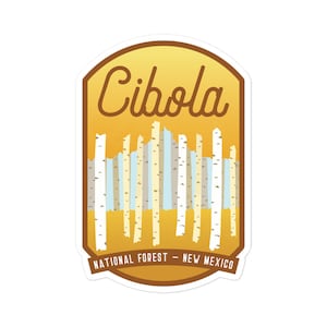May include: A yellow and brown sticker with the text "Cibola National Forest - New Mexico". The sticker features a stylized image of a forest with trees.