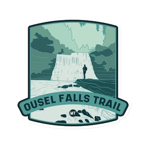 May include: A green and blue illustrated sticker of a waterfall with a hiker standing on a rock in the foreground. The text "OUEL FALLS TRAIL MT" is printed on the sticker.