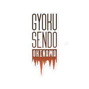 May include: A white sticker with the words "GYOKU SENDO OKINAWA" in a brown, bold font. The bottom of the sticker has a dripping design in shades of orange and brown.