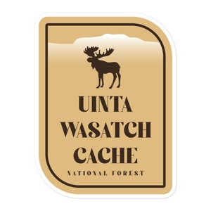May include: A sticker featuring a brown moose silhouette above the words "Uinta Wasatch Cache National Forest." The design is set on a tan background with a brown border and the text is in a serif font.