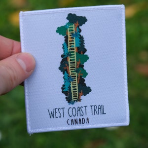 May include: White embroidered patch with a green, blue, and yellow illustration of a forest trail. The text "WEST COAST TRAIL CANADA" is printed below the illustration.