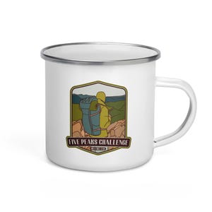 Pode incluir: Caneca de acampamento de esmalte branco com uma ilustração verde, marrom e amarela de um caminhante com uma mochila no topo de uma montanha. O texto "Five Peaks Challenge - Ire. & Ireland" está impresso na caneca.