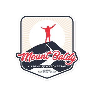 Könnte beinhalten: Ein Aufkleber mit einer roten Silhouette einer Person auf einem Berg, mit den Worten "Mount Baldy" in roter Schrift. Das Design enthält den Text "Via Devil's Backbone Trail" und "Angeles National Forest."