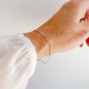 May include: A silver chain bracelet with a delicate, twisted design. The bracelet is shown on a person's wrist.