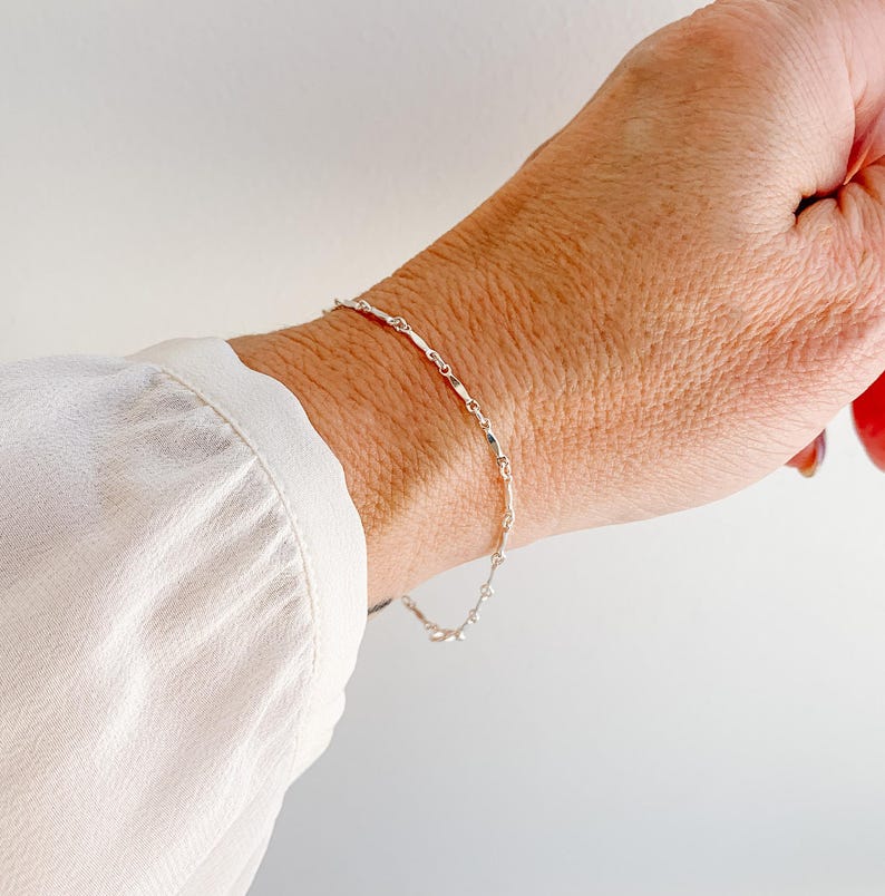 May include: A silver chain bracelet with a delicate, twisted design. The bracelet is shown on a person's wrist.