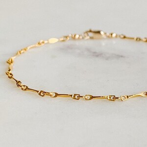May include: A delicate gold chain bracelet with a simple, elegant design. The chain is made of small, linked pieces that create a subtle wave pattern.