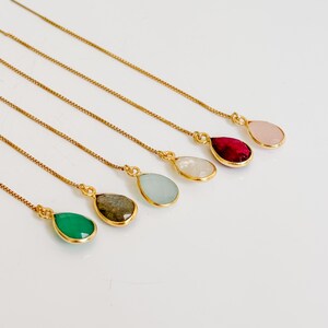 May include: Six gold-tone chain earrings, each featuring a single teardrop-shaped gemstone pendant. The stones are in various colours including green, grey, light blue, white, deep red, and pale pink, all set in gold-tone metal frames.