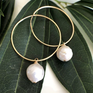 Peut inclure: Une paire de boucles d'oreilles créoles en or avec une perle blanche suspendue à chaque créole.