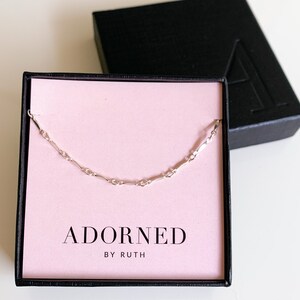 May include: A silver chain necklace in a pink box with the text "ADORNED BY RUTH".