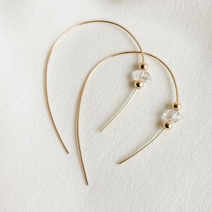 May include: A pair of gold hoop earrings with clear crystal accents. The hoops are thin and delicate, and the crystals are faceted and sparkly.