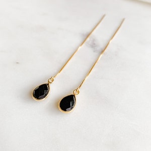 May include: A pair of gold dangle earrings with black teardrop-shaped stones.