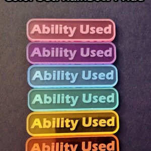 May include: Six acrylic tokens in rainbow colors, each with the text "Ability Used" printed in white.