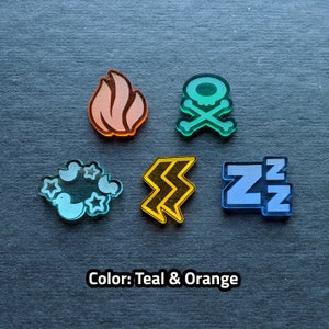 Puede incluir: Cinco fichas de acr&iacute;lico de color turquesa y naranja con diferentes s&iacute;mbolos. Los s&iacute;mbolos son una llama, una calavera y huesos cruzados, un rayo, una nube con p&aacute;jaros y estrellas, y las letras ZZZ.
