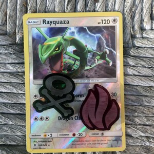 Puede incluir: Una carta de Pok&eacute;mon Rayquaza con un fondo verde y rojo. La carta presenta una criatura verde de tipo drag&oacute;n con ojos rojos y un s&iacute;mbolo de calavera rojo y negro. La carta tiene el texto "Rayquaza" y "Dragon Claw".