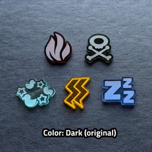 Puede incluir: Cinco fichas acr&iacute;licas de diferentes colores con varios s&iacute;mbolos. Las fichas son una llama rosa claro, una calavera y huesos cruzados grises, una nube azul claro con p&aacute;jaros, un rayo amarillo y un s&iacute;mbolo 'ZZ' azul. Las fichas est&aacute;n sobre un fondo gris oscuro. Color: Oscuro (original)