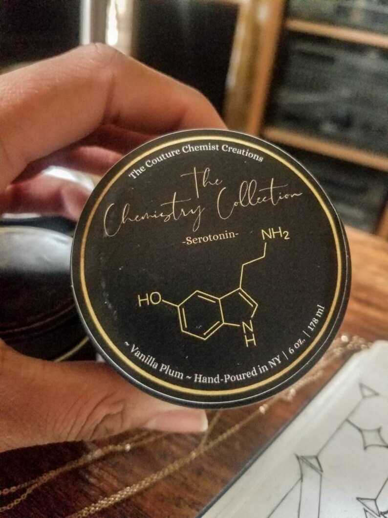 May include: A black and gold label with the text "The Couture Chemist Creations The Chemistry Collection -Serotonin- NH2 ~Vanilla Plum ~ Hand-Poured in NY | 6 oz. | 178 ml" and a chemical structure diagram.