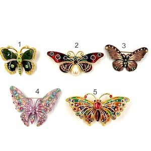 May include: Five different butterfly brooches with colourful enamel and rhinestones. The butterflies are in various colours, including green, red, brown, pink, and orange.